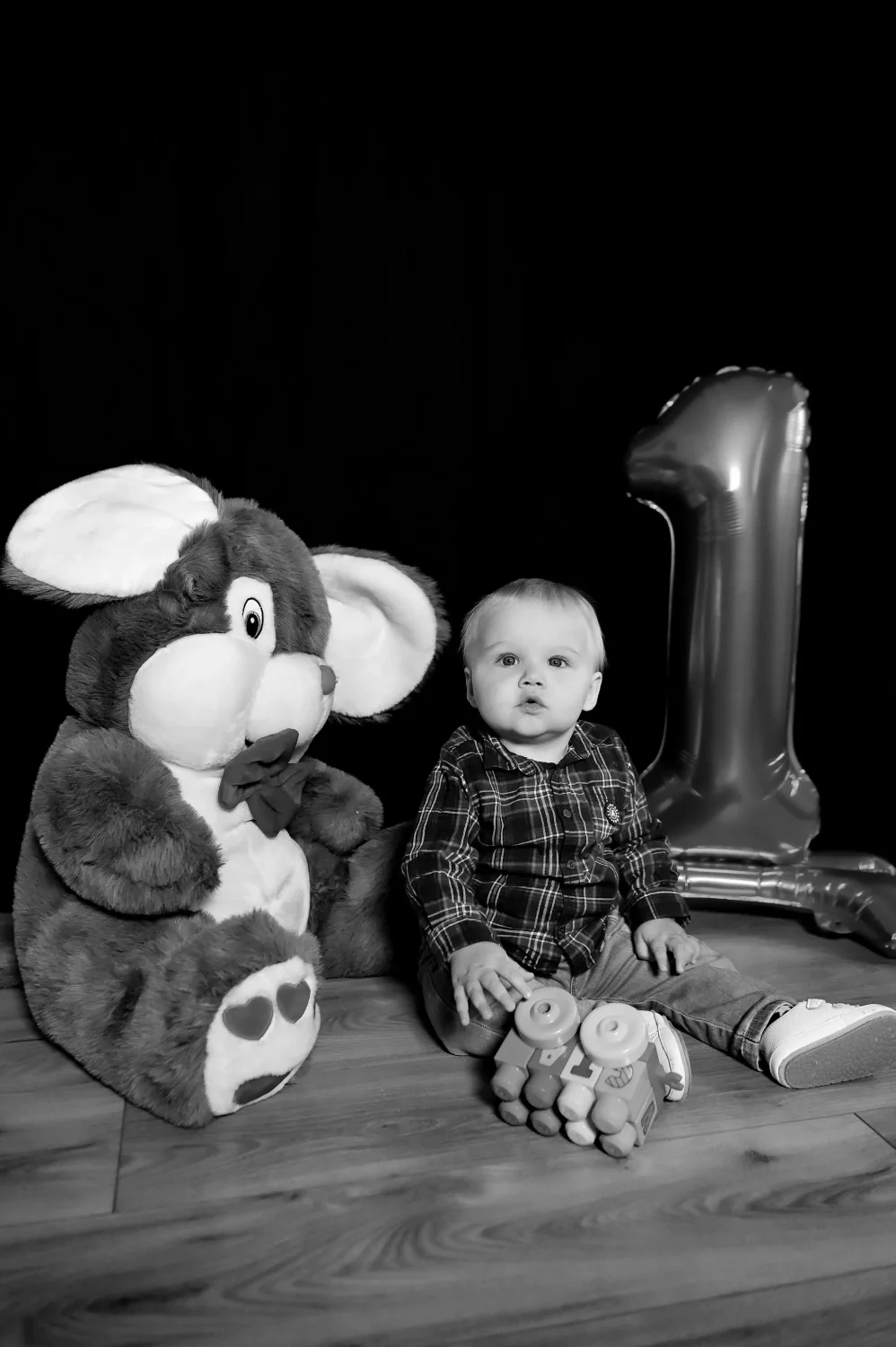 Bébé fêtant son premier anniversaire à côté d'une grande peluche, photo en noir et blanc