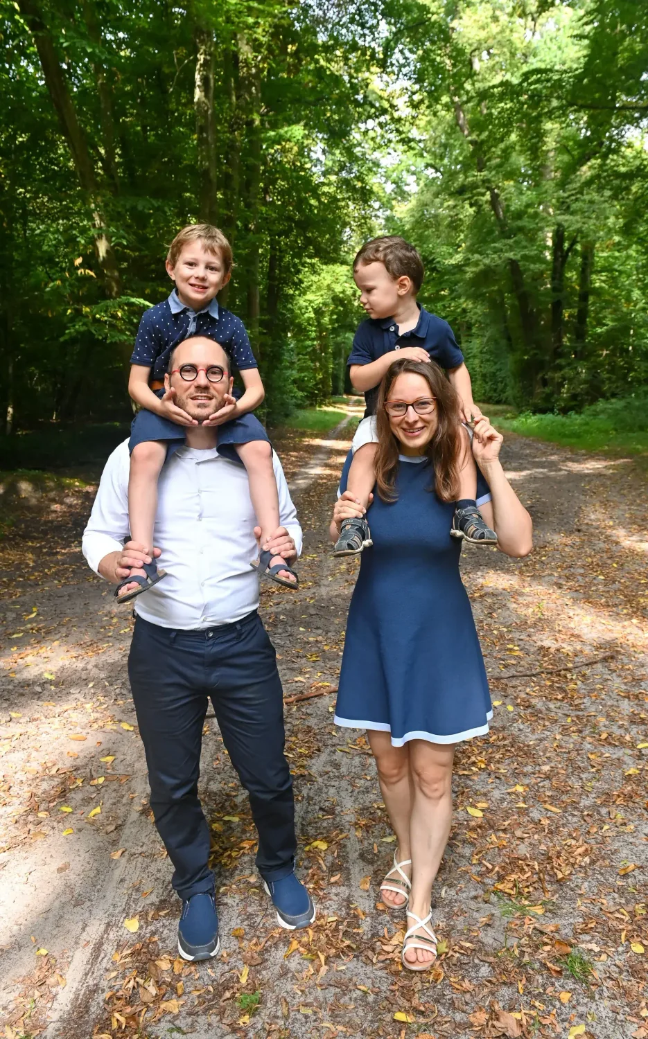 Parents portant leurs enfants sur les épaules dans une allée en forêt
