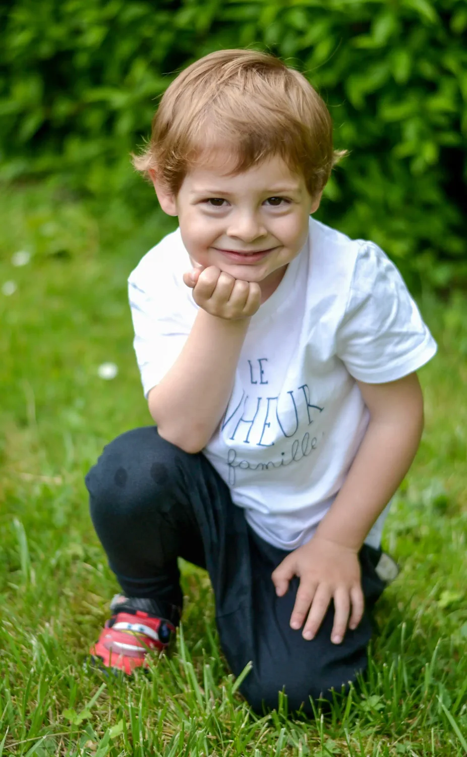 Petit garçon souriant accroupi dans l'herbe, séance photo enfant en extérieur