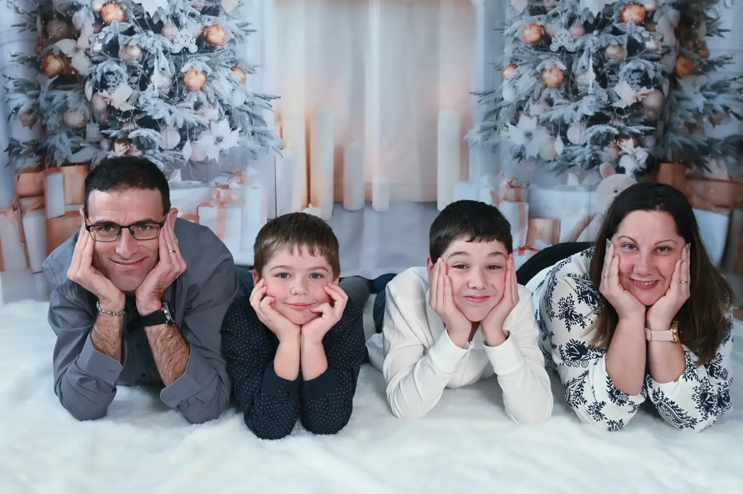 Famille de quatre allongée devant un décor de sapins, séance photo de Noël