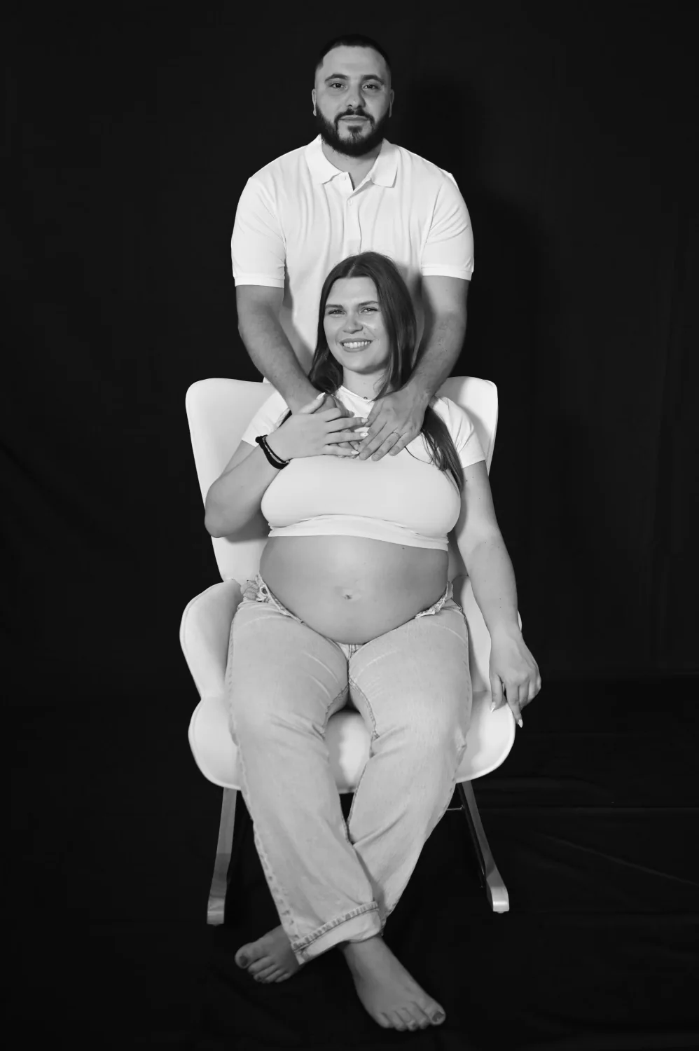 Future maman assise et futur papa derrière elle, séance grossesse en studio