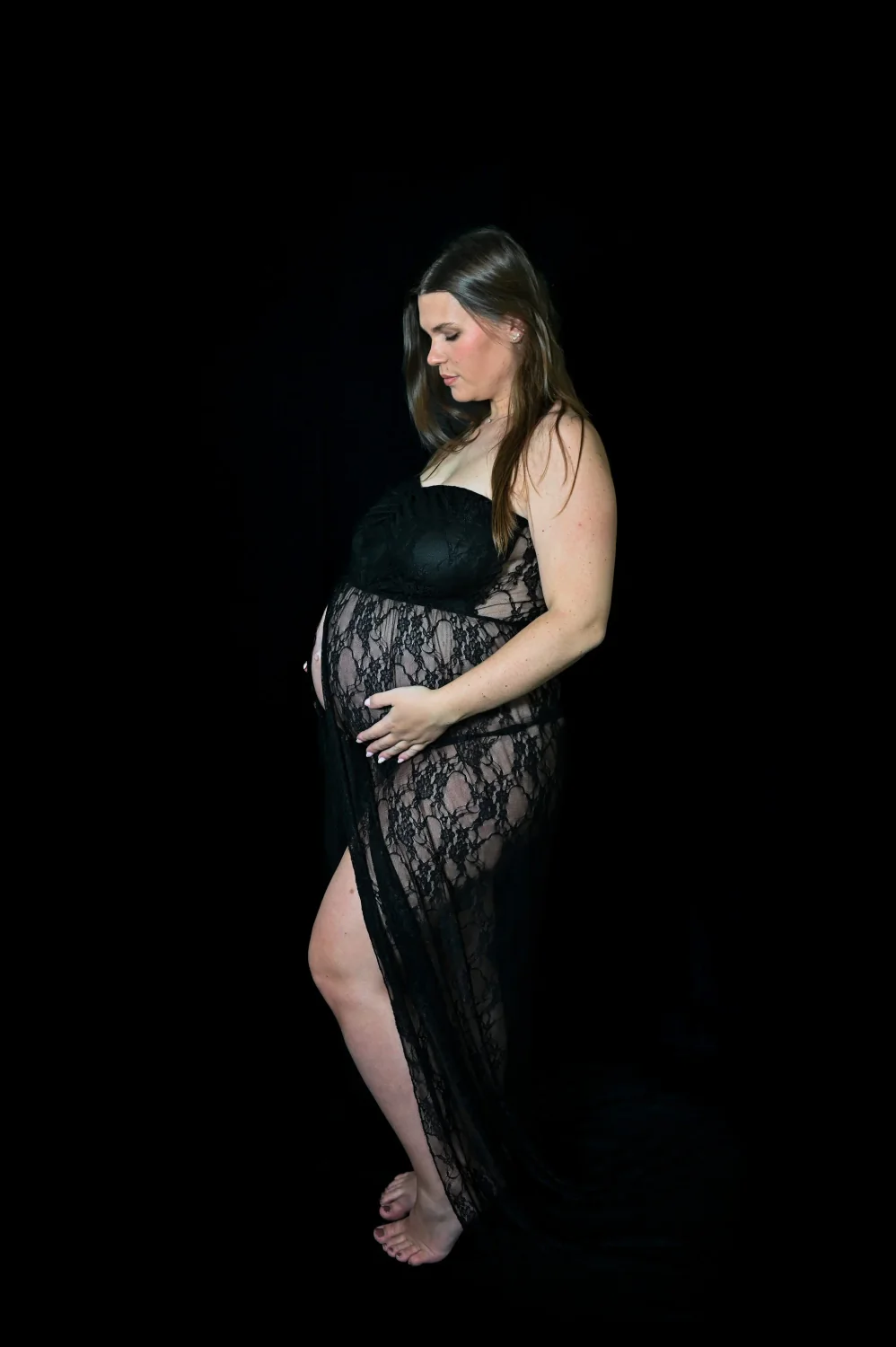 Future maman en robe de dentelle noire sur fond noir, séance grossesse en studio