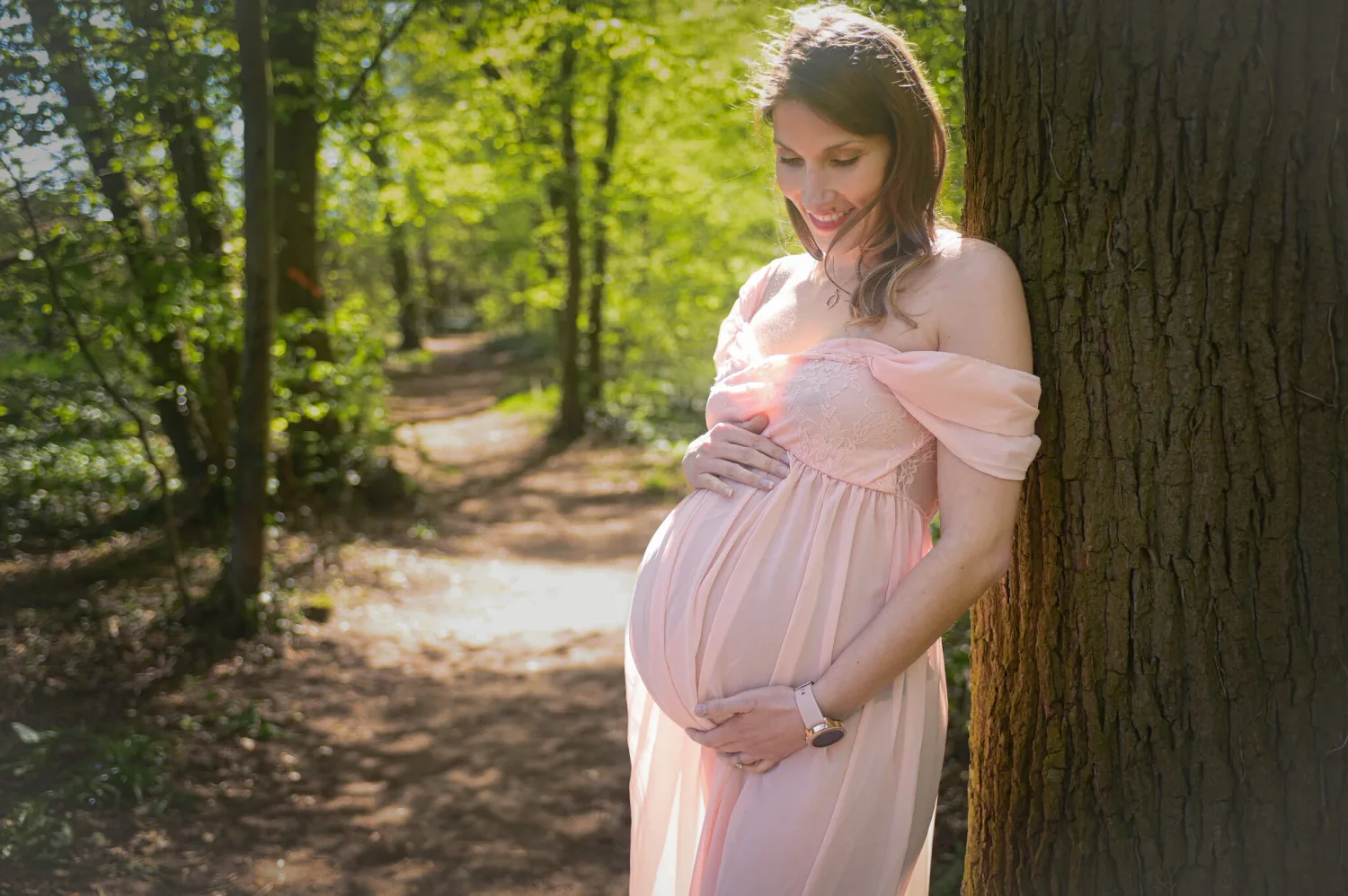 Future maman en robe rose dans une forêt lumineuse, séance grossesse en extérieur