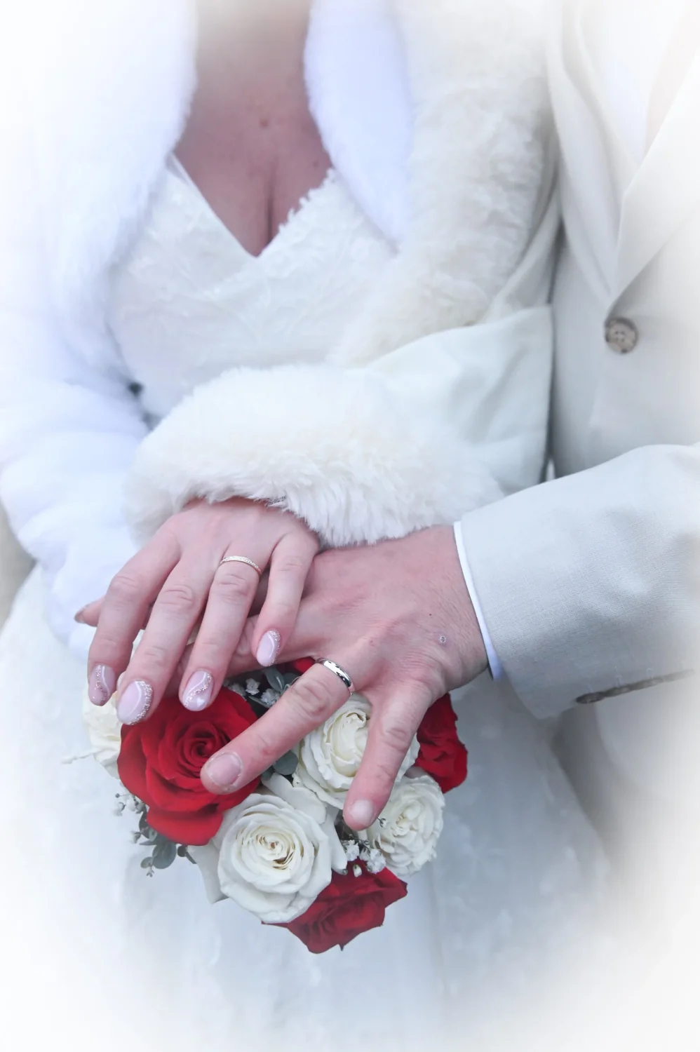 Mains des mariés avec alliances posées sur un bouquet de roses