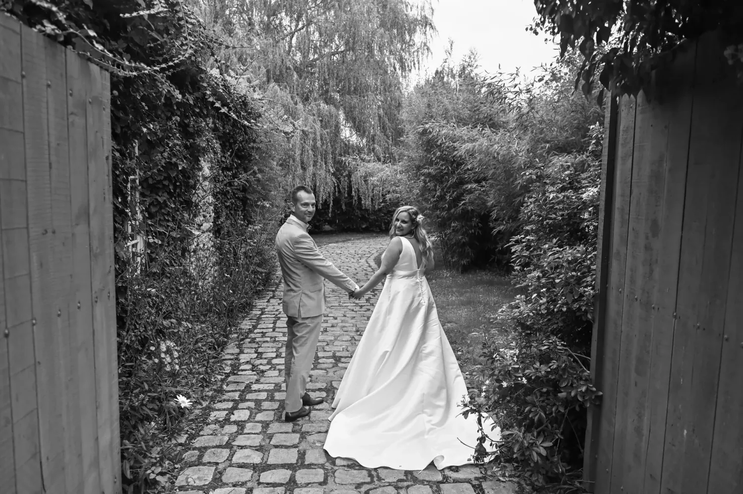 Mariés main dans la main dans une allée de jardin, en noir et blanc