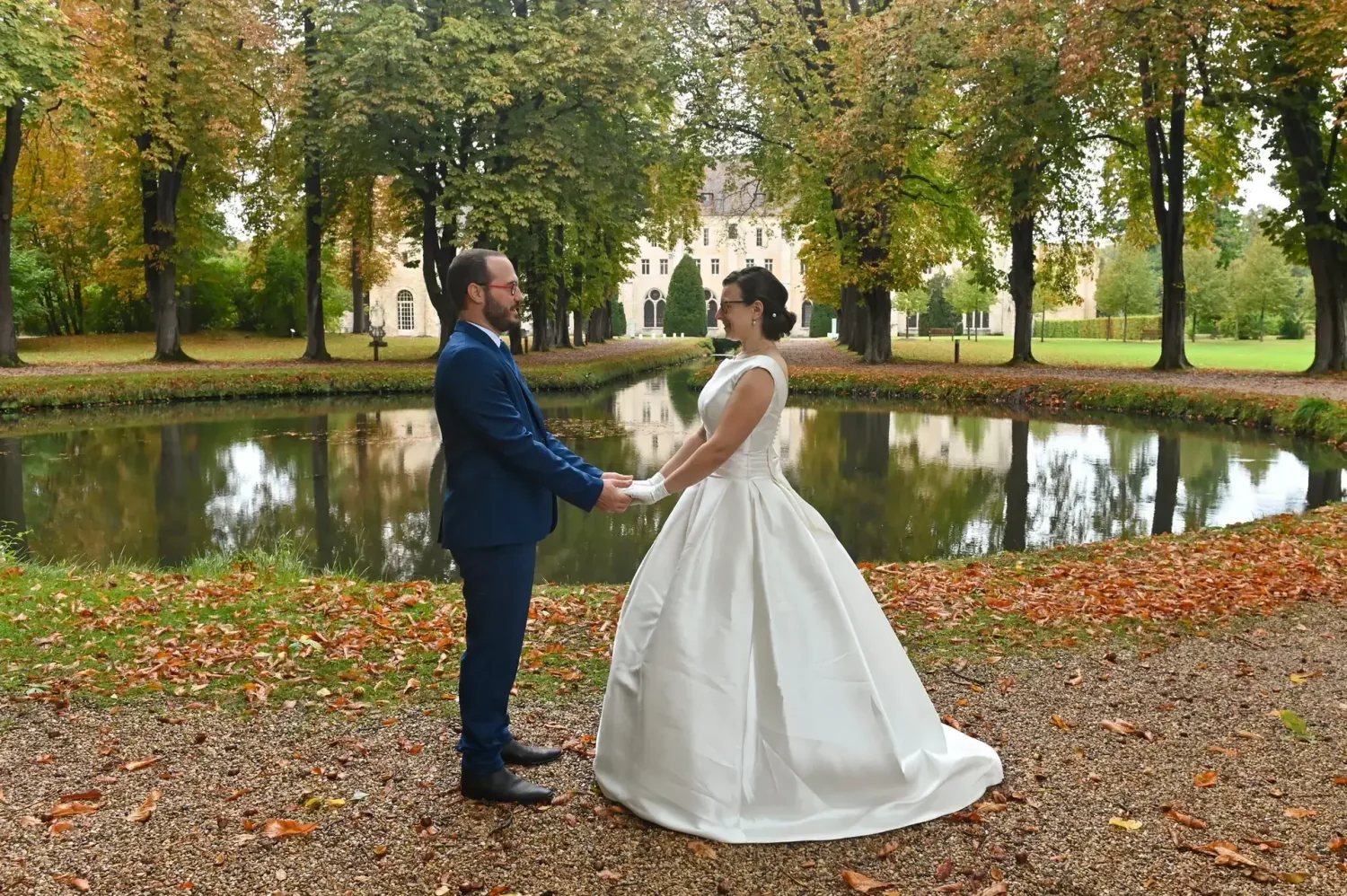 Mariés main dans la main au bord d'un étang en automne
