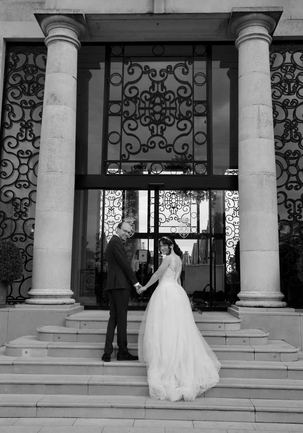 Mariés sur les marches d'une grande porte en fer forgé, en noir et blanc