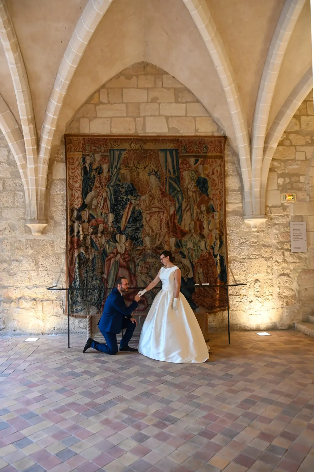 Marié à genoux devant la mariée dans une salle ornée d'une tapisserie