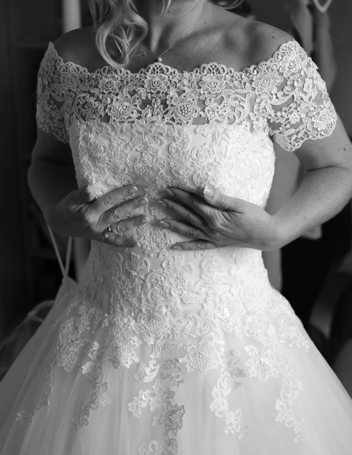 Détail d'une robe de mariée en dentelle, mains croisées, en noir et blanc