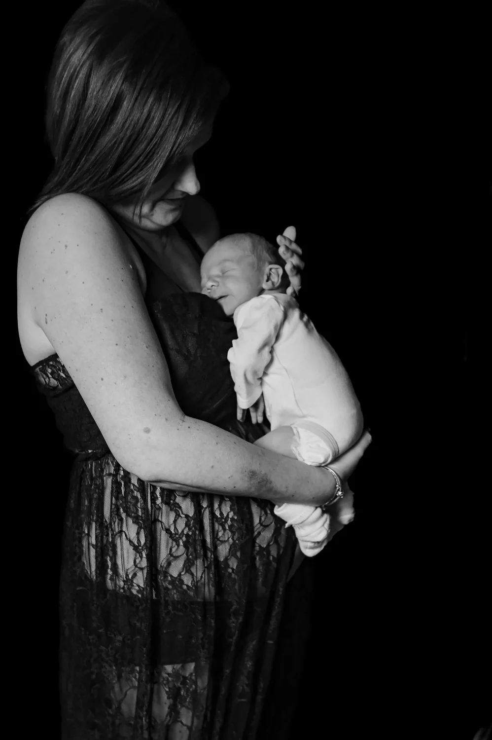 Maman en dentelle tenant son nouveau-né contre elle, en noir et blanc